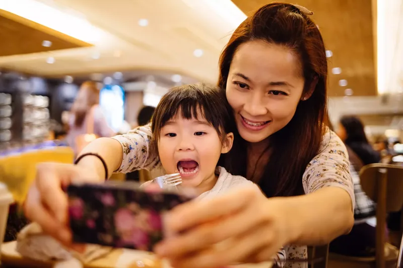 Mom & toddler girl taking selfie joyfully in cafe