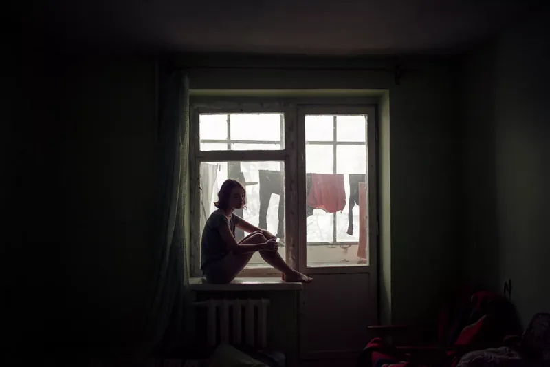 Depressed woman sits in a dark rooms by the window