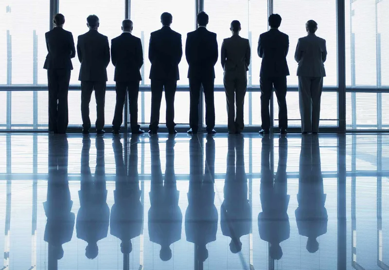 Silhouette of business people in a row looking out lobby window