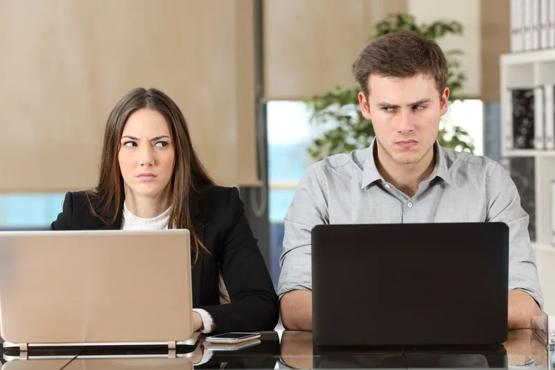 Upset woman and man sitting side by side working on laptops