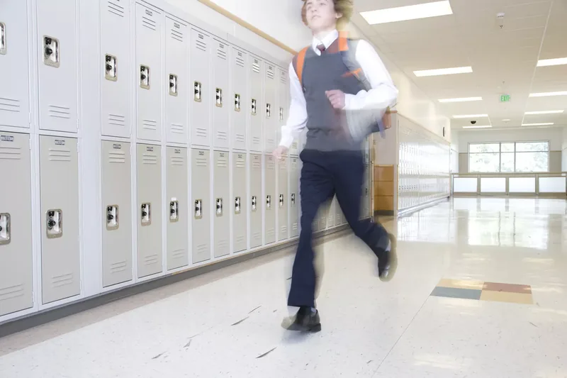 School boy (16-17) running past lockers in corridor