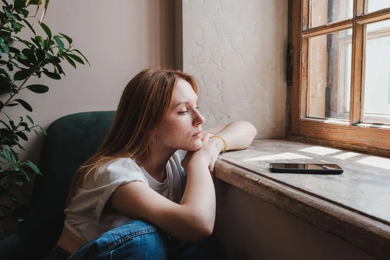 A person resting by a windowsill next to a smartphone looking outside