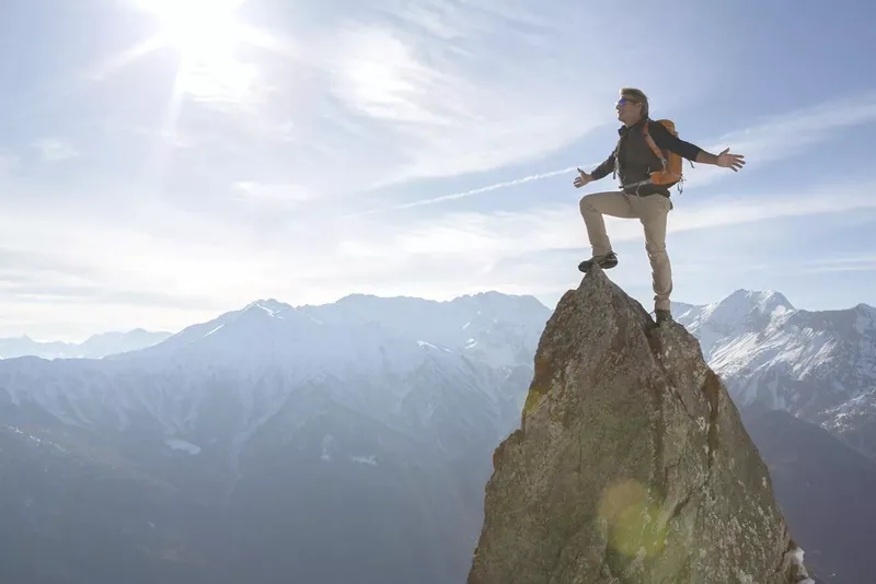 Hiker stands on pinnacle summit, arms outstretched