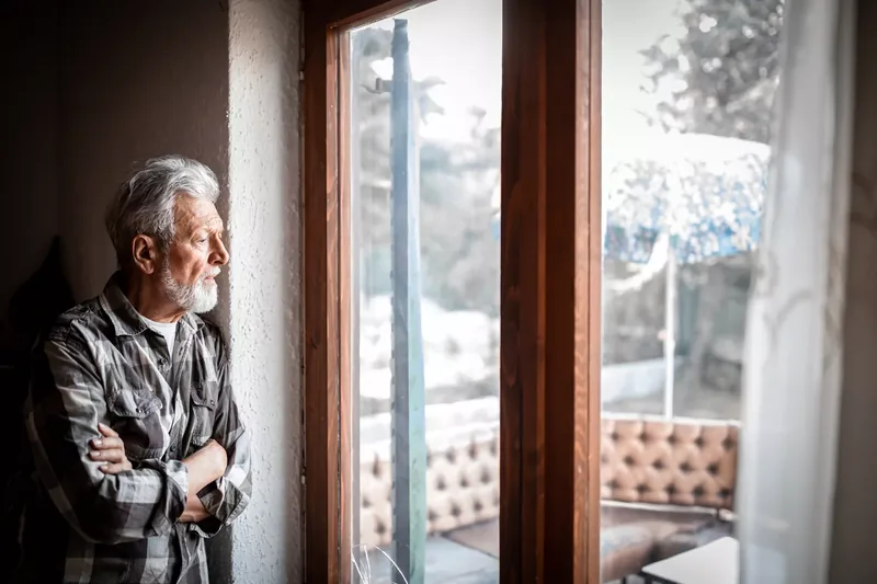 Portrait of older adult man lost in thought looking out a window