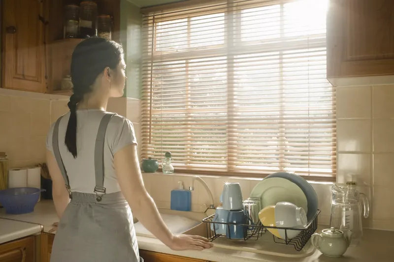 Woman doing dishes looking out window.