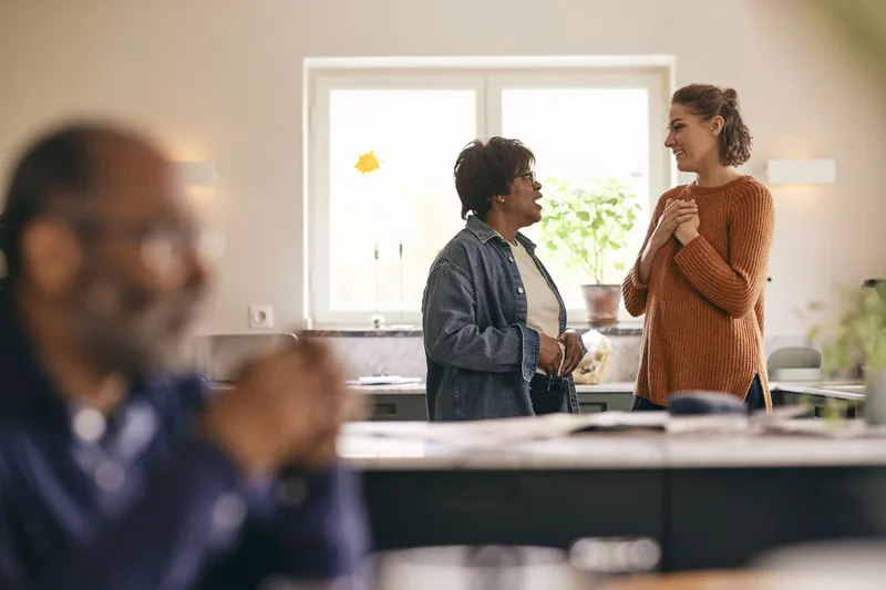 Woman with hands on chest talking to mother-in-law standing in kitchen at home