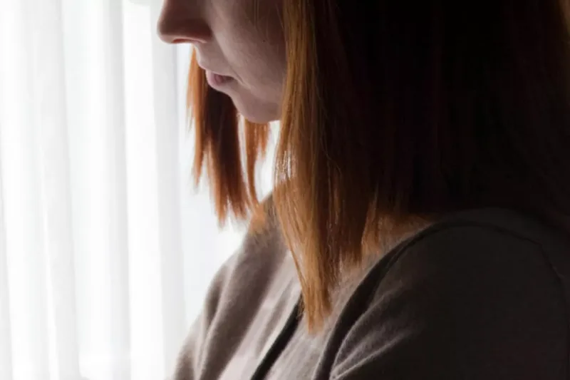 Woman standing near bedroom window, arms crossed