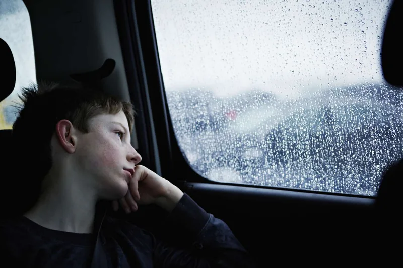 Young boy looking out rainy car window