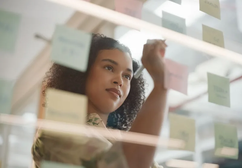 A person arranging sticky notes on a glass board