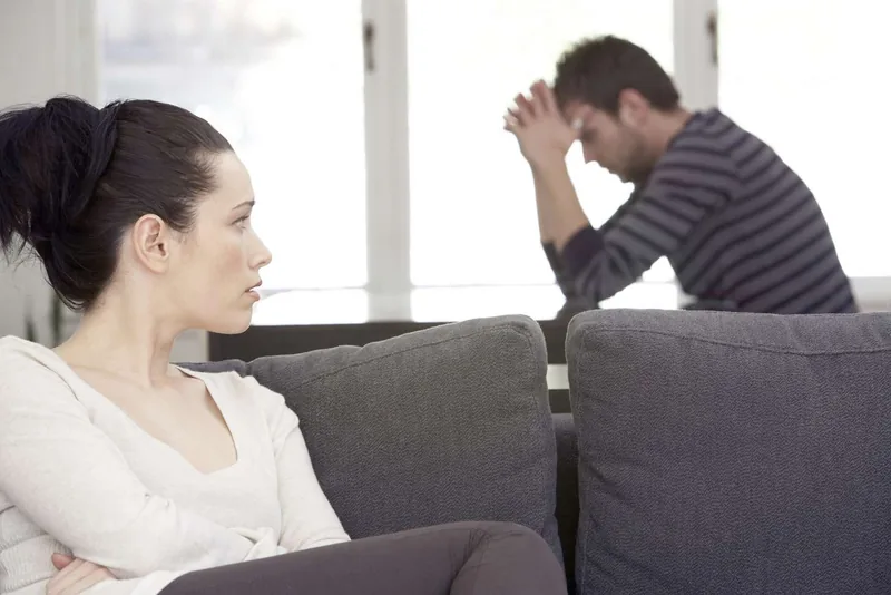 Young woman sitting on sofa, looking at distressed man at table