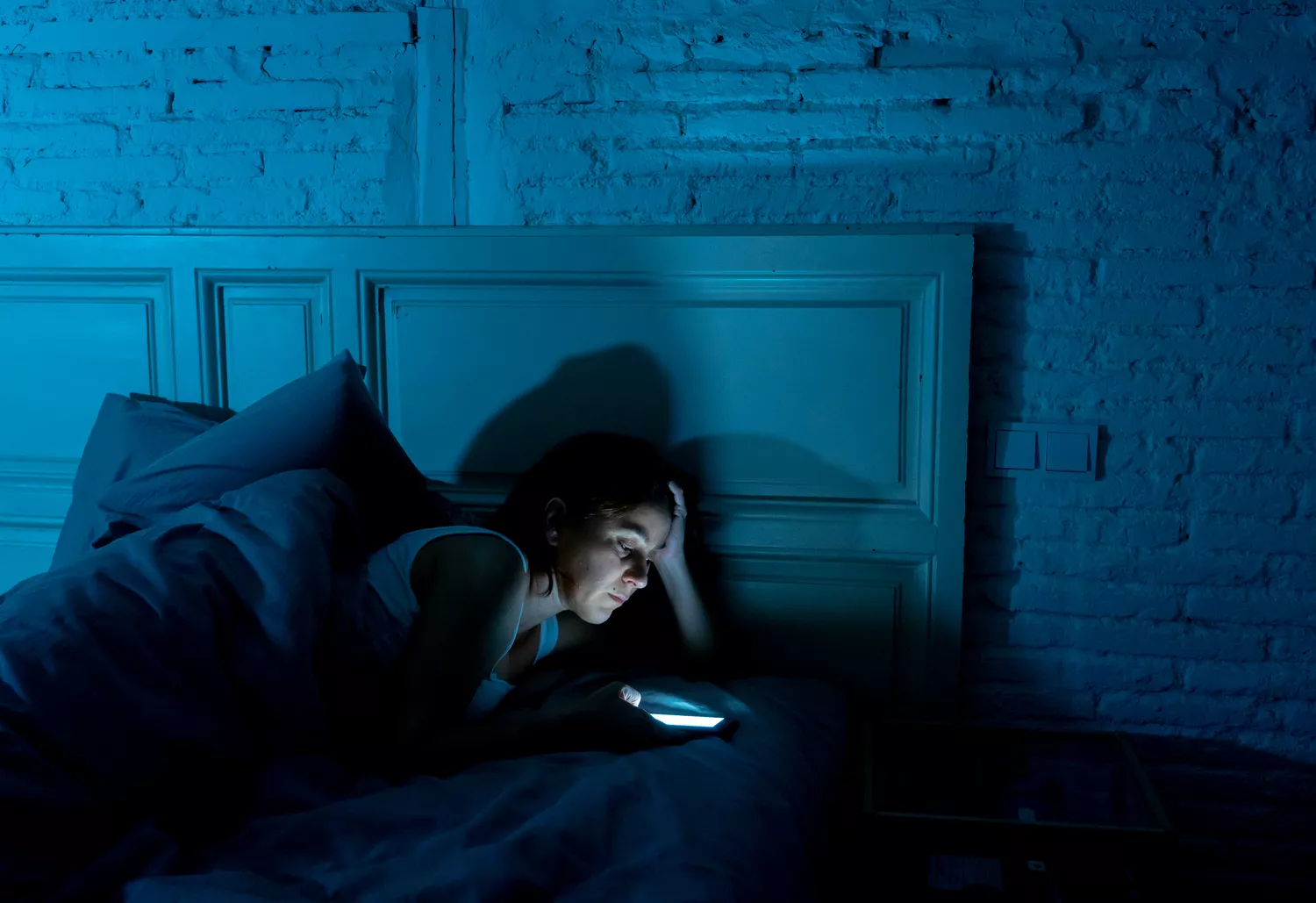 Addicted young beautiful woman chatting and surfing on the internet using her smart phone sleepy bored and tired late at night in mobile addiction concept and insomnia