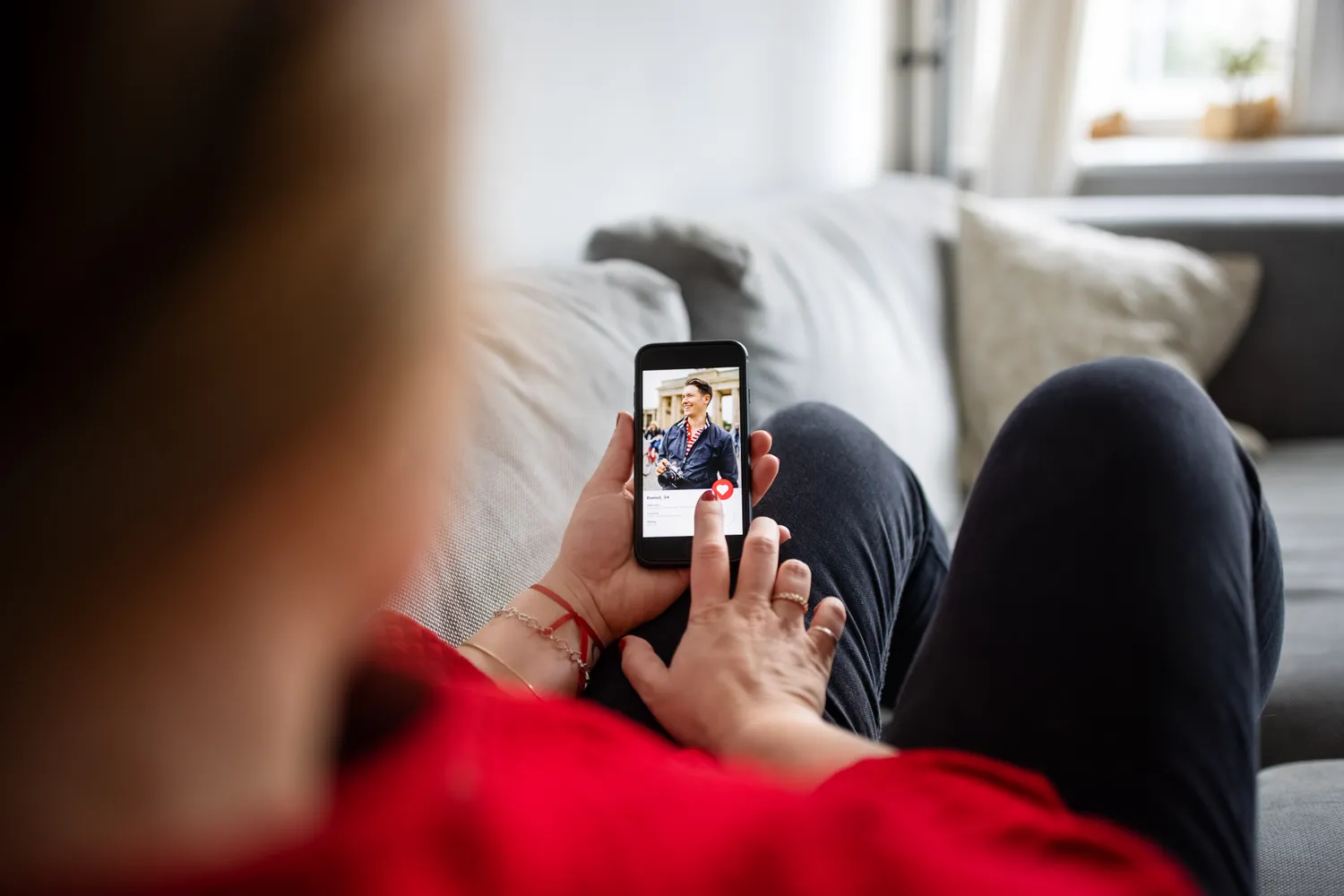 A person looking at a dating app on a smartphone while reclining on a couch