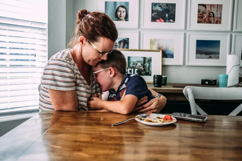 mom hugging sad young boy at dinner table