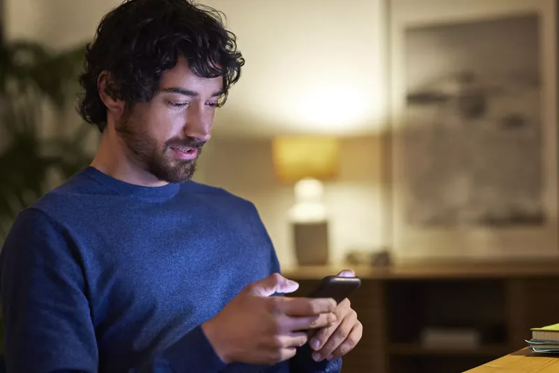 Handsome businessman using smart phone at home. Male professional is looking at mobile phone. He is working late