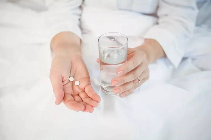 woman in bed taking medication with water