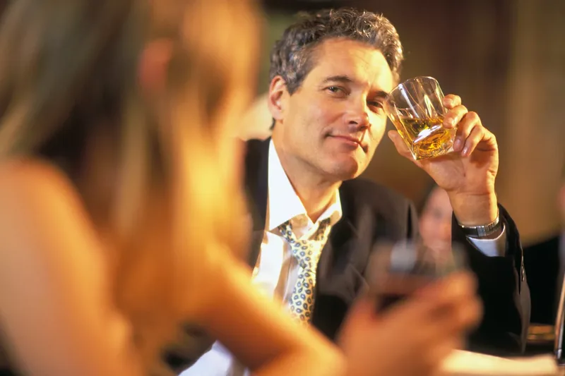 white man at a bar holding his drink up to a woman