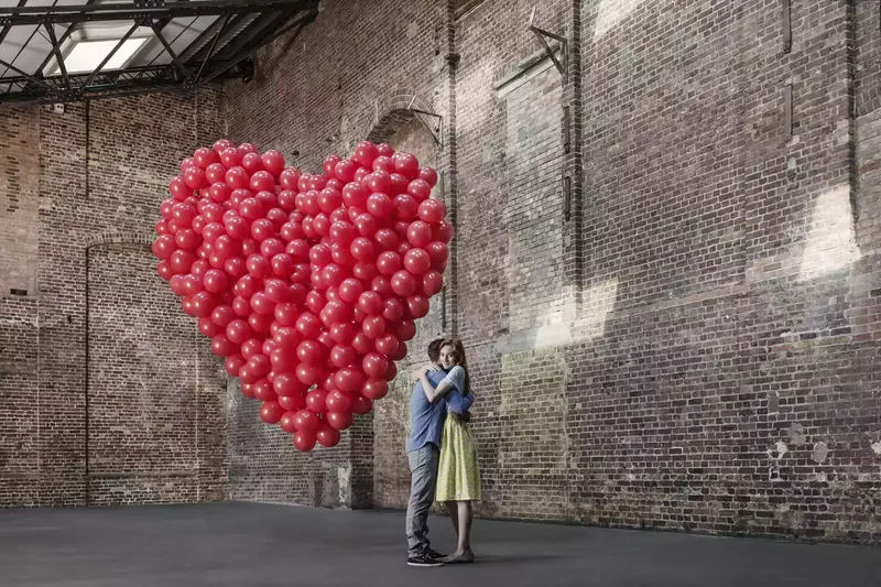 man and woman hugging in a warehouse with a group of red balloons shaped like a heart