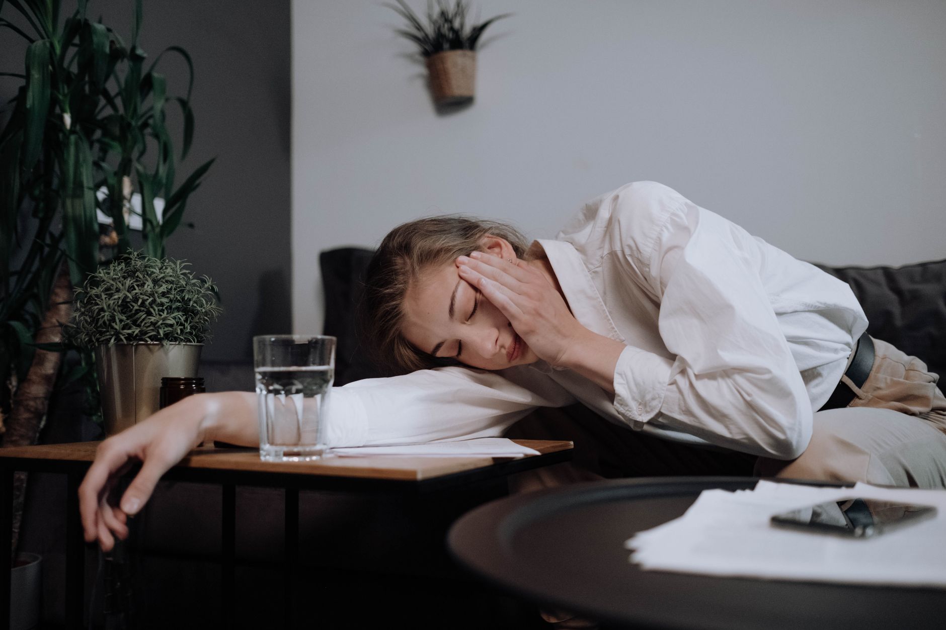 A tired woman in business attire resting with her head on a table in a cozy home setting.