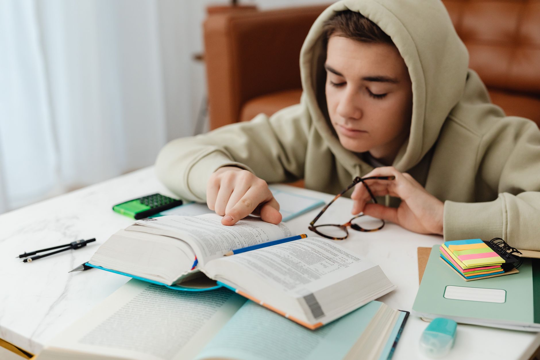 A teenager in a hoodie studying with books and notes on a table, focused on learning indoors.