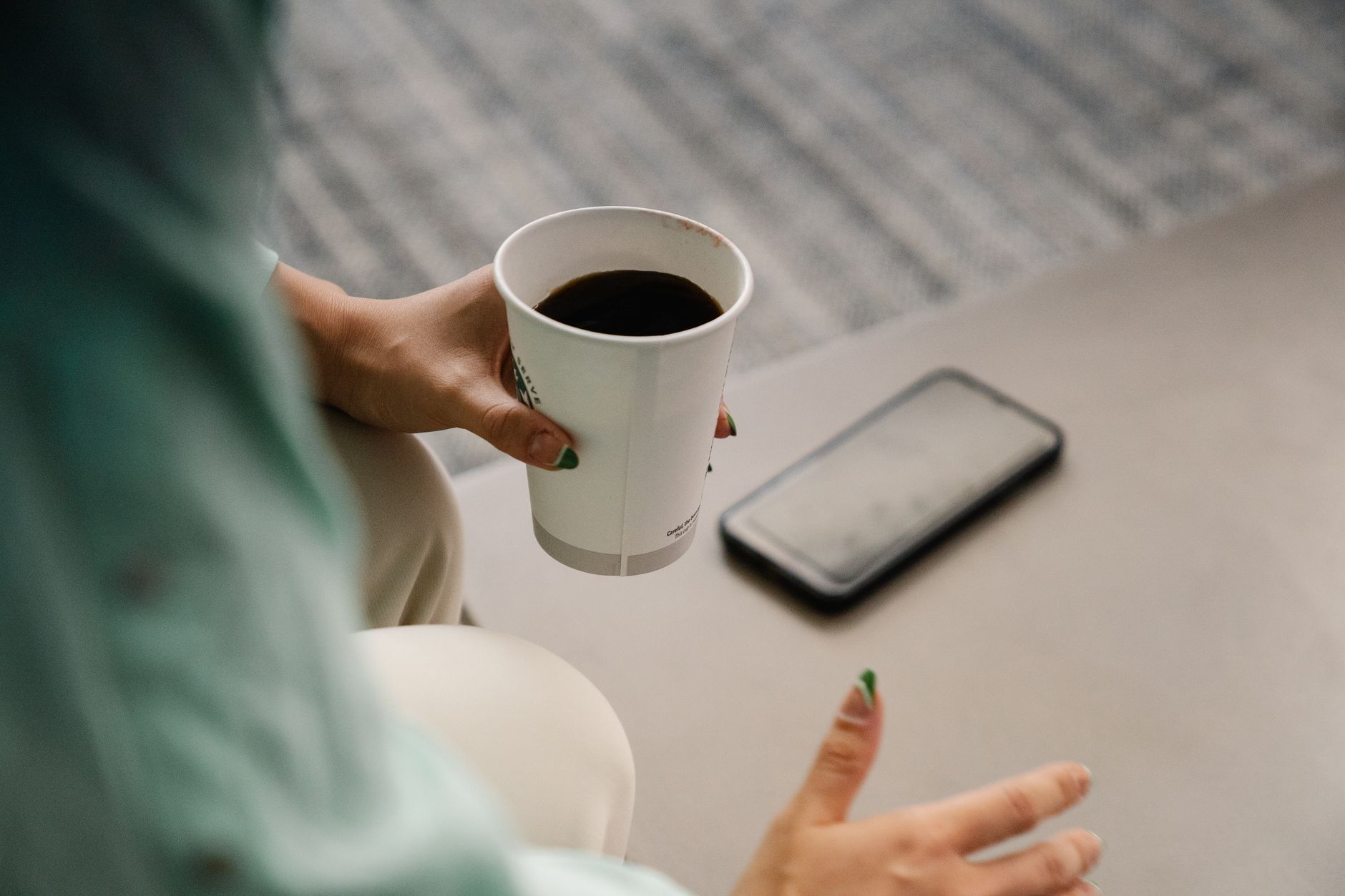 Woman holding a paper coffee cup with smartphone nearby in a relaxed setting.
