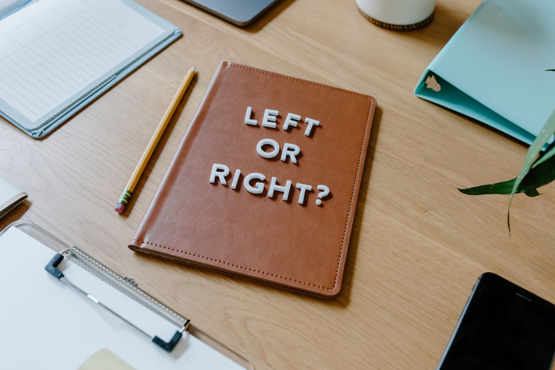 Top-down view of a desk with a notebook asking 'Left or Right?' and various office supplies.