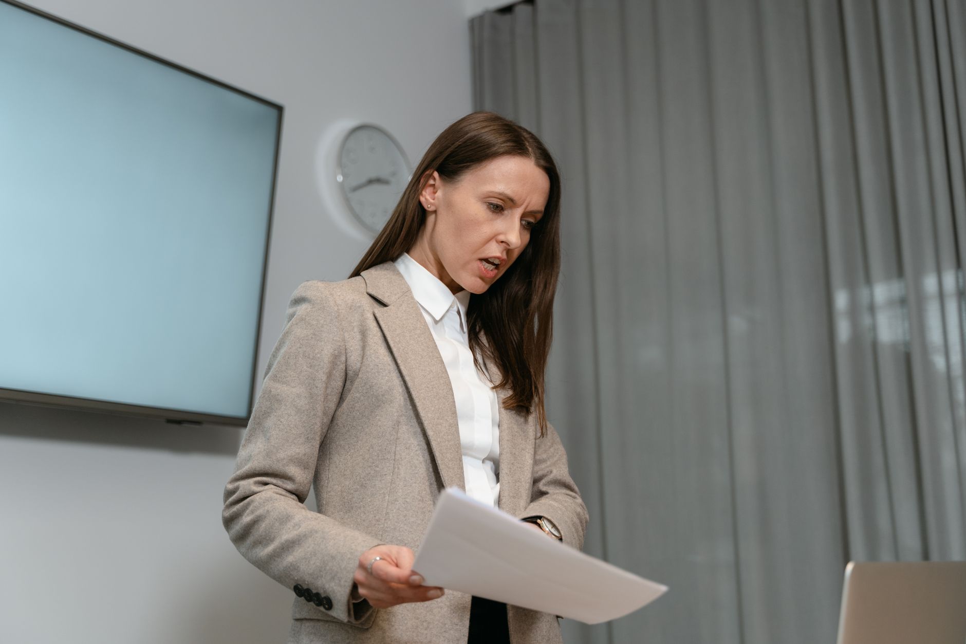 Professional woman in business attire reviewing documents indoors during a daytime meeting.