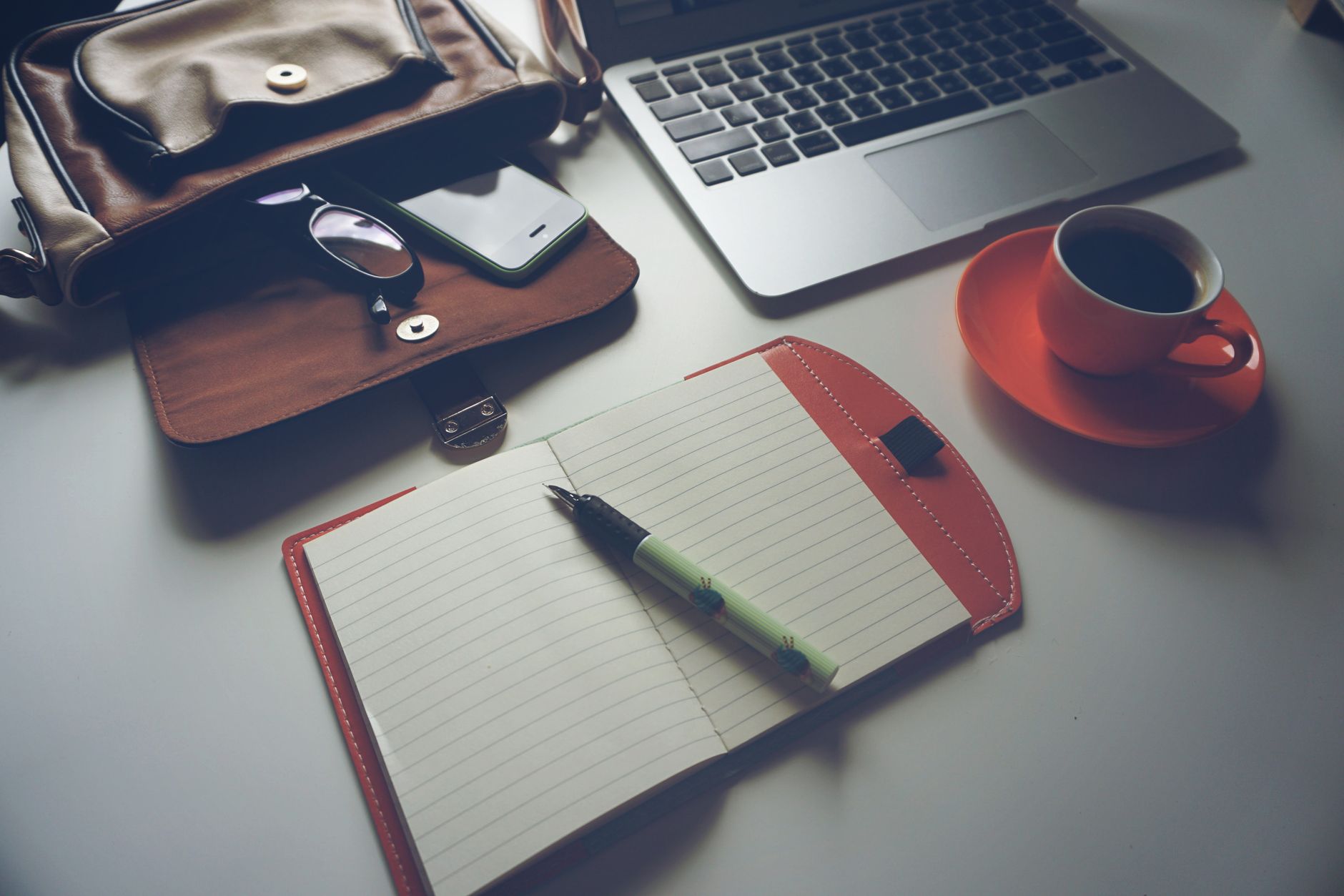 Stylish office workspace featuring a notebook, pen, laptop, and coffee cup on a tidy desk.