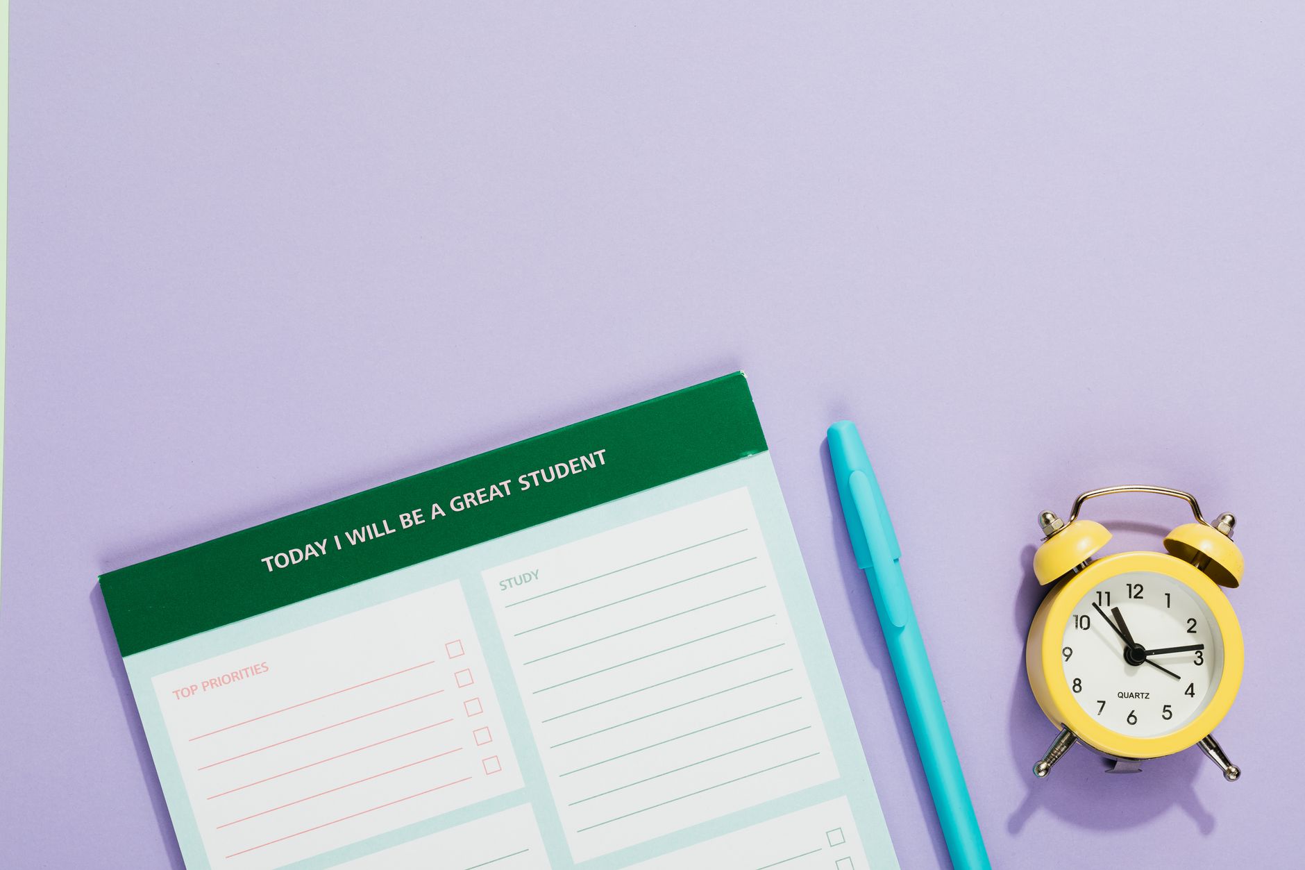 A vibrant still life with a motivational student planner, pen, and yellow alarm clock on a pastel backdrop.