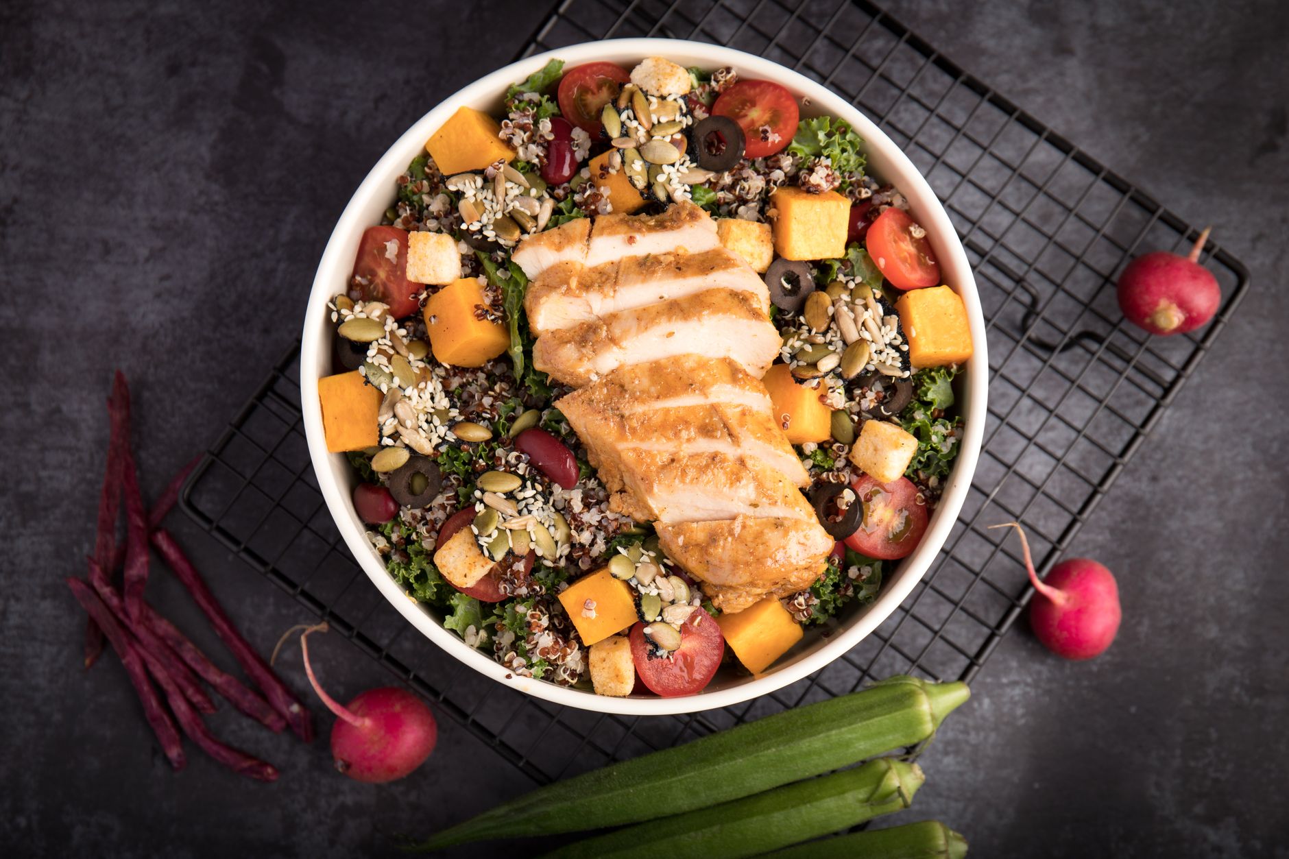 A vibrant bowl of grilled chicken salad with quinoa, fresh vegetables, and seeds.