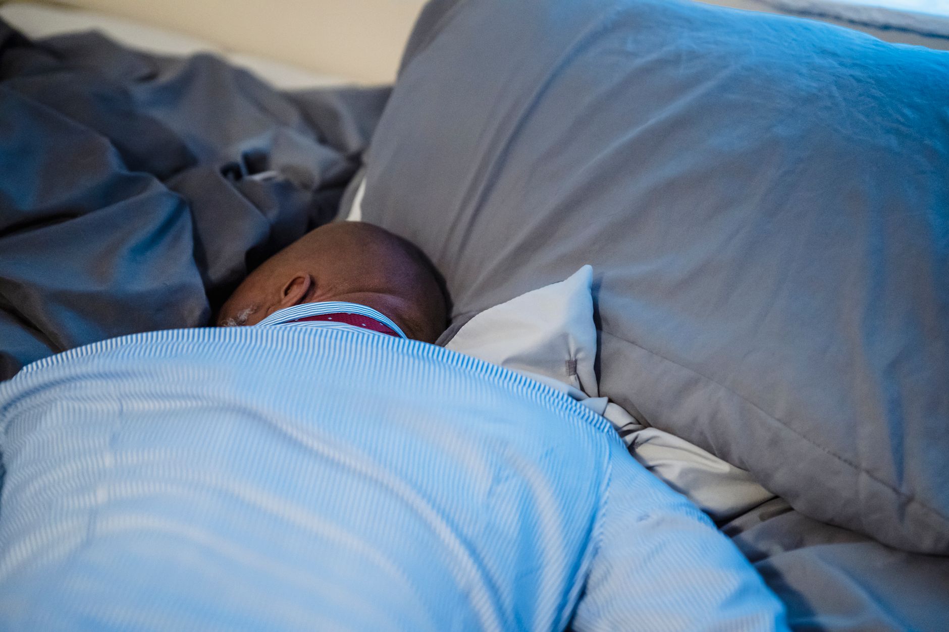 An adult resting peacefully on a bed with soft gray bedding, captured in an indoor setting.