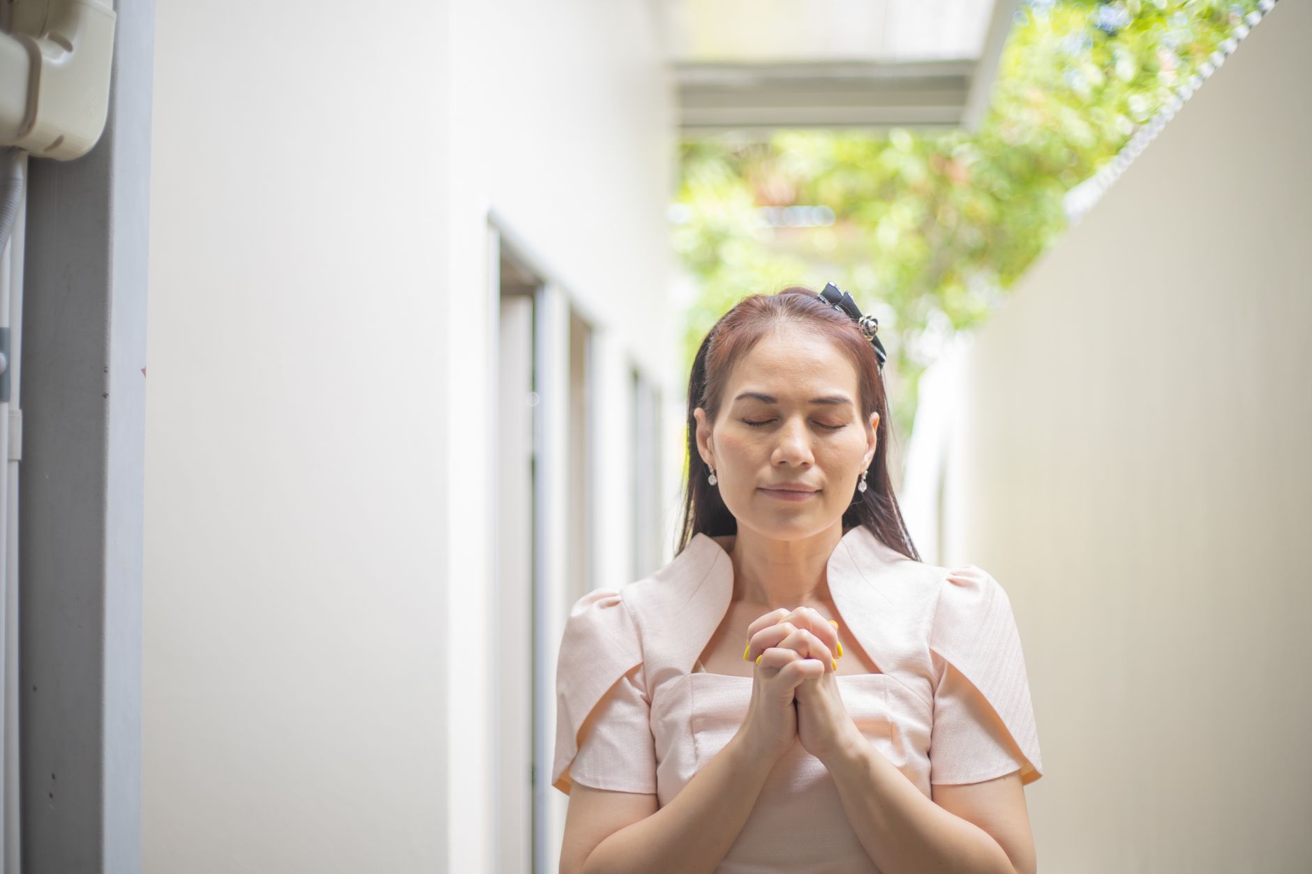 A serene woman with eyes closed, standing outdoors and clasping her hands in prayer, projecting calm and peace.