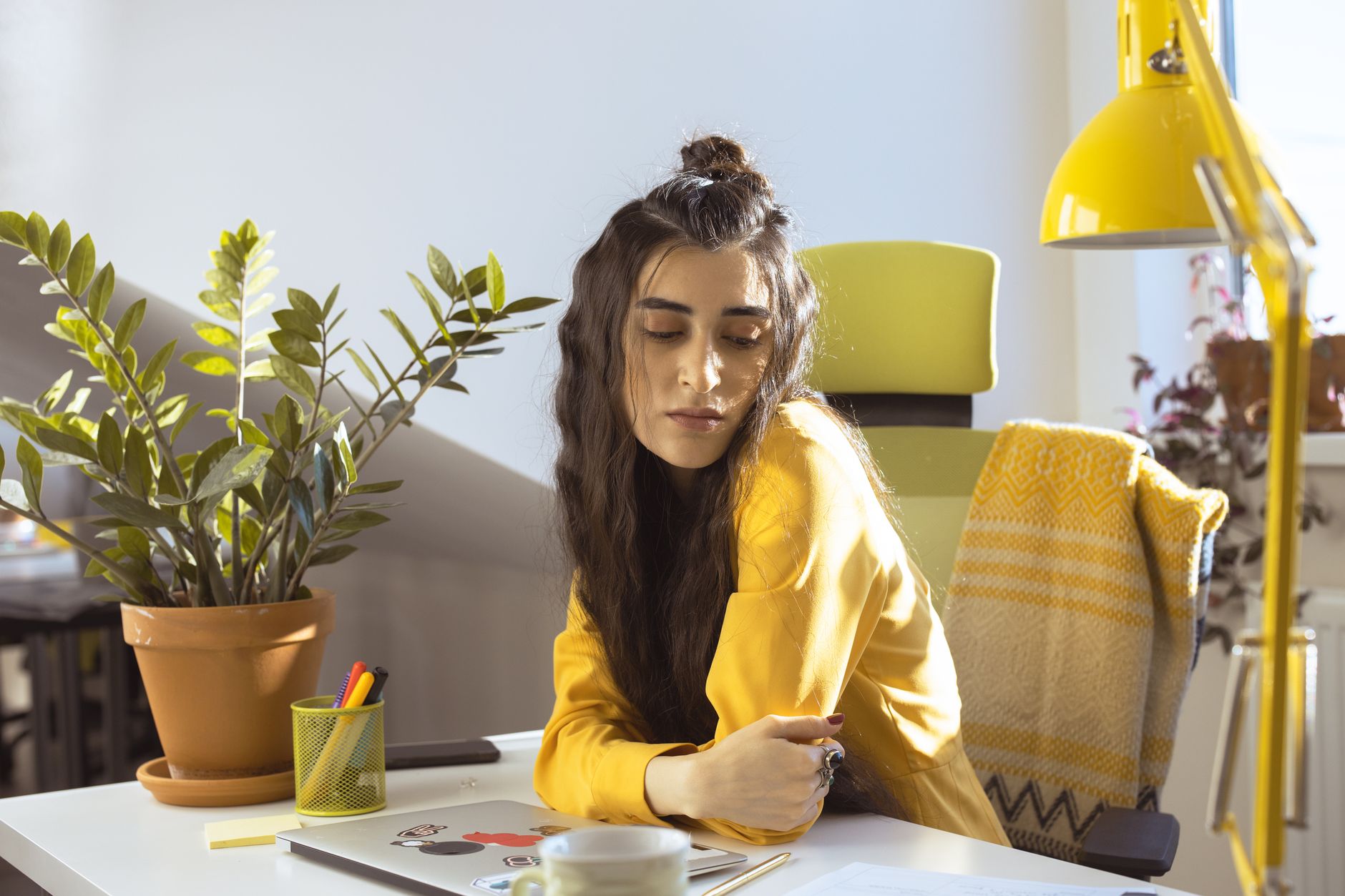 Woman in yellow sweater working in a sunlit office with plants.