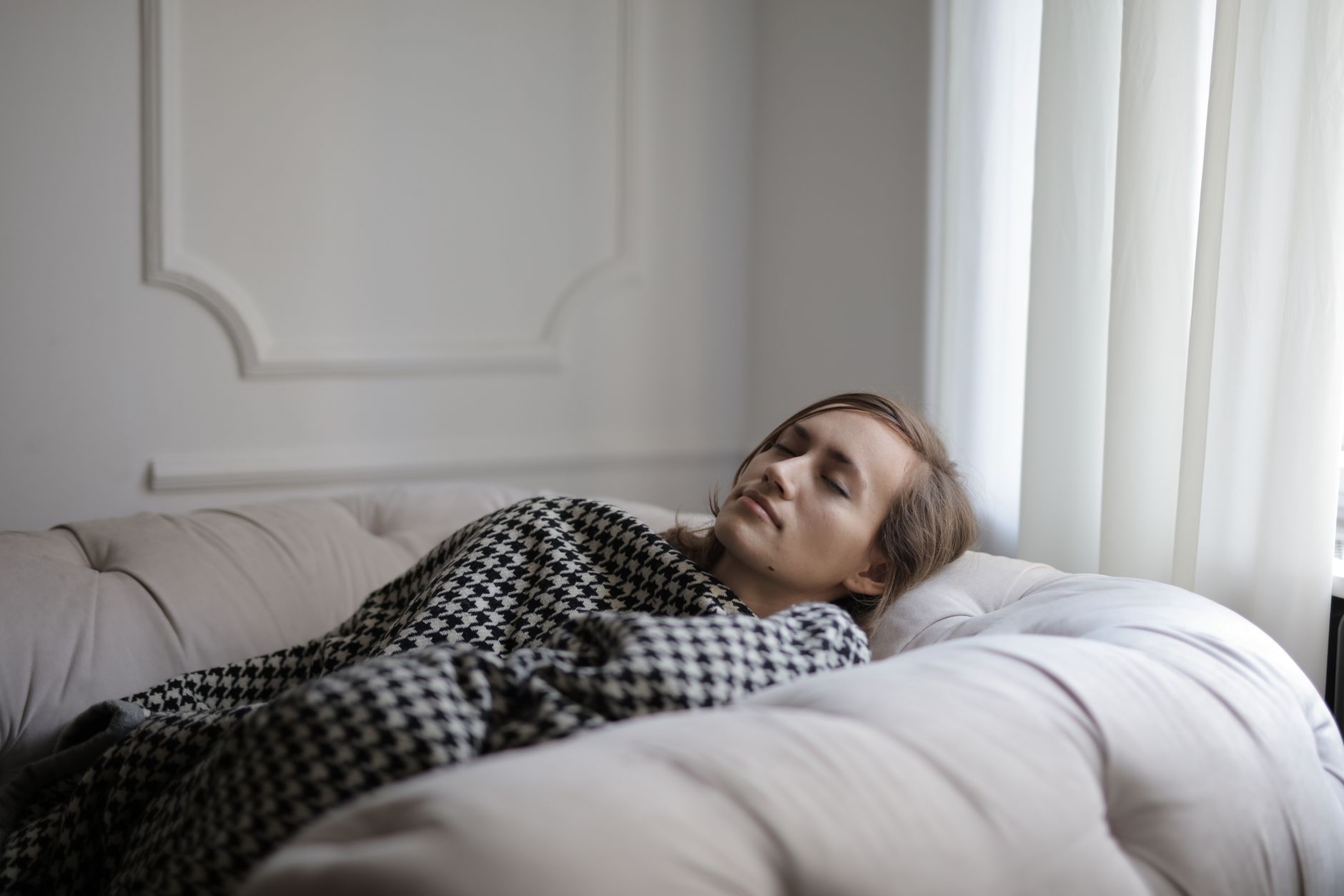 A woman peacefully resting on a couch with a checked blanket, showcasing relaxation.
