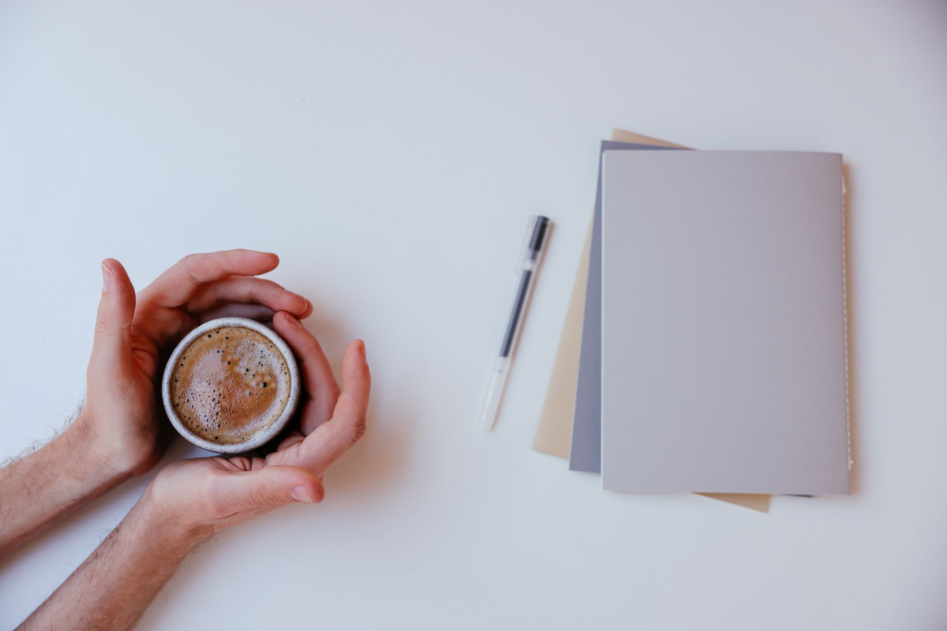 A warm coffee surrounded by notebooks and pen on a white background, perfect for productivity.