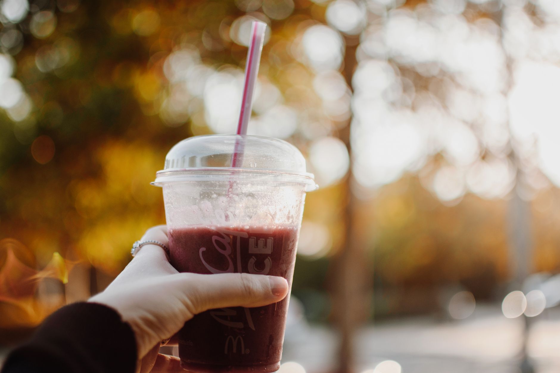 Close-up of a hand holding a berry smoothie cup outdoors at sunrise with a warm bokeh background.