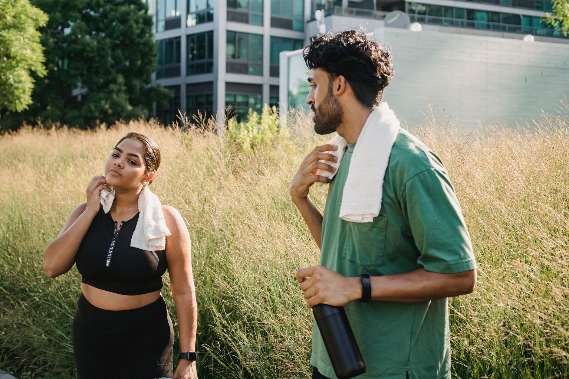 Two adults cooling down after exercise in an urban park setting, enjoying a summer day.