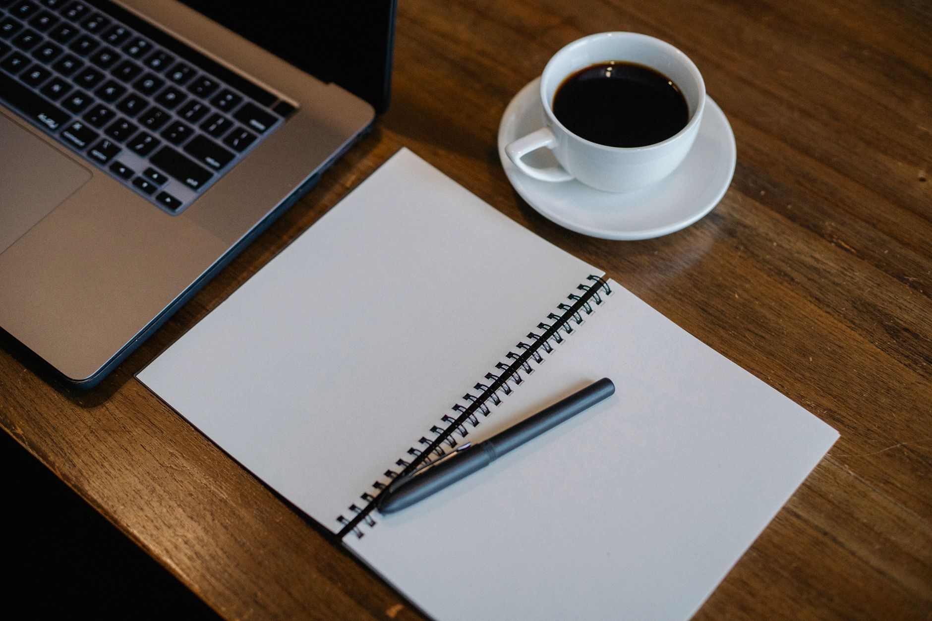 From above of workspace with cup of hot coffee and pen on empty notepad near modern laptop on wooden table