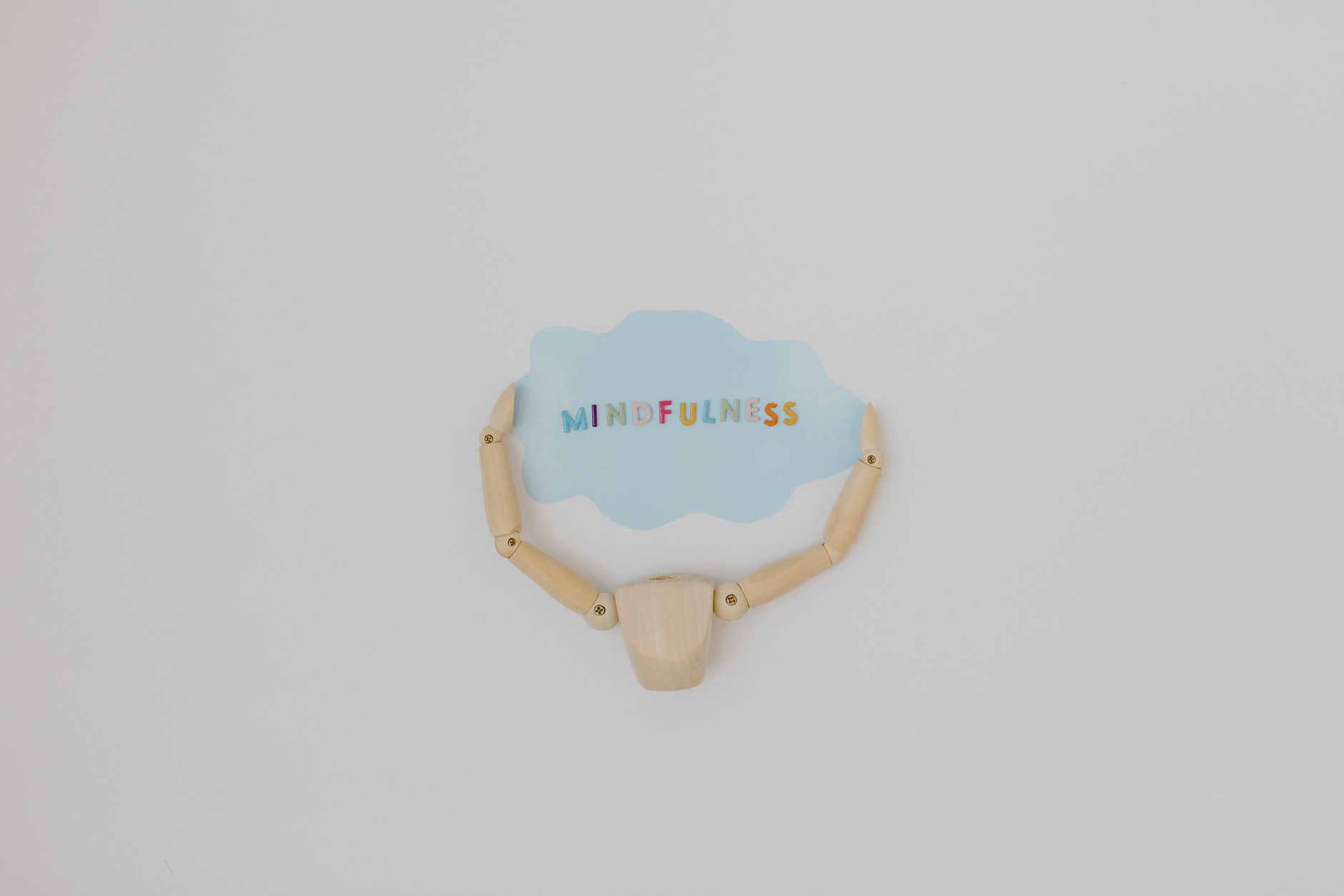Minimalist image of a wooden figure holding a speech bubble saying 'Mindfulness'.