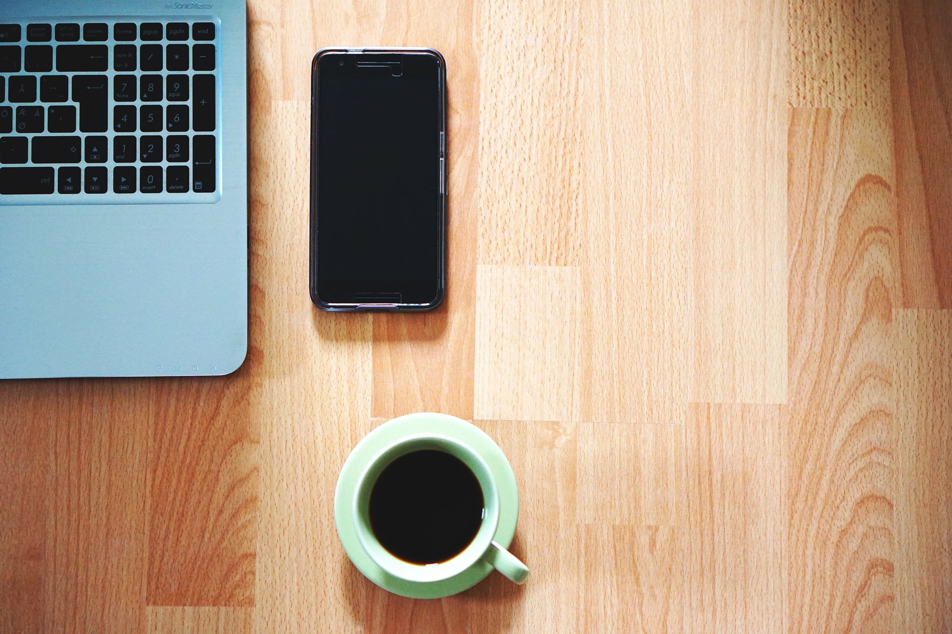 A tidy workspace with a laptop, smartphone, and coffee cup on a wooden desk.