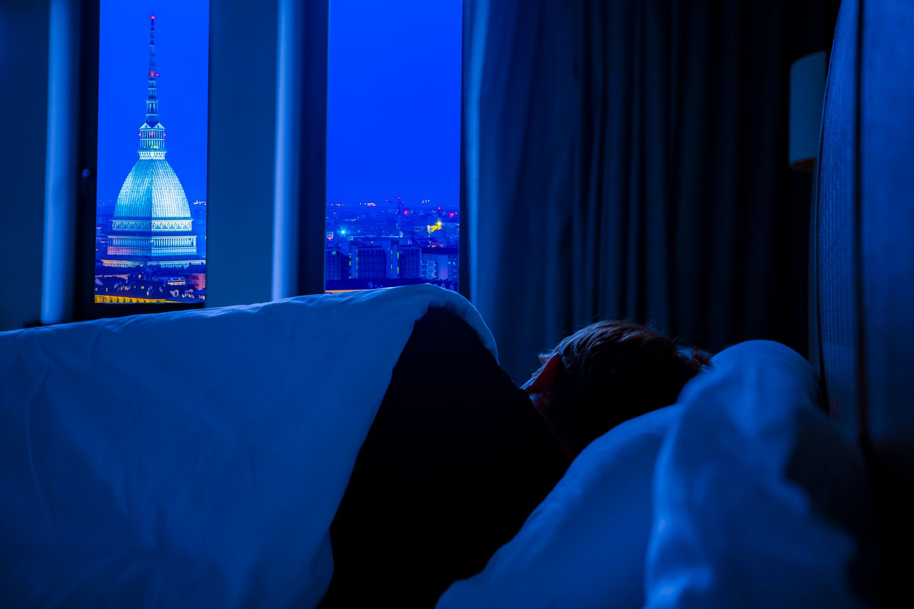 A serene view of Turin's night skyline featuring Mole Antonelliana, seen from a cozy bedroom.